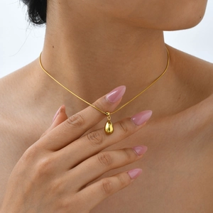 Close-up of a minimalist gold teardrop pendant on a fine snake chain necklace
