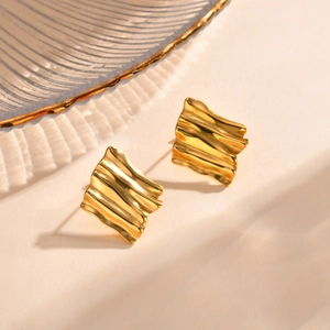 Detailed close-up of golden wavy square stud earrings with textured metallic finish