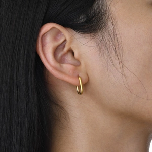 Gros plan d'une boucle d'oreille créole rectangulaire dorée portée par un mannequin