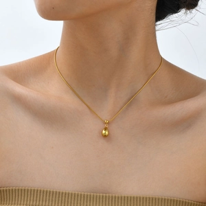 Close-up of a minimalist golden water drop pendant on a sleek snake chain necklace