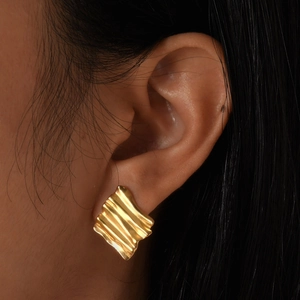 Close-up of golden geometric pleated earrings showing modern irregular wavy texture on ear