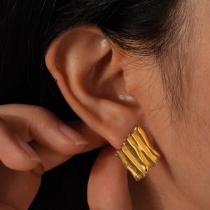 Macro view of gold rectangular stud earrings with vertical wavy pleated metal texture
