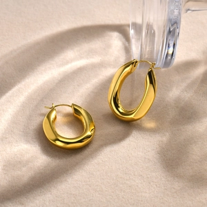 Detailed close-up of polished gold U-shaped hoop earrings on a textured sand background