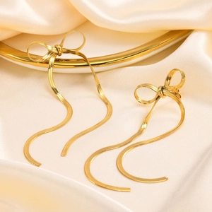 Detailed shot of golden bow earrings with long tassel snake chains on silk fabric