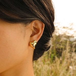 Close-up of polished golden heart stud earrings worn by a model in soft natural sunlight