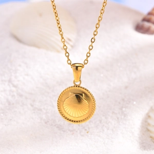 Close-up of golden shell pendant necklace on white beach sand with natural seashells
