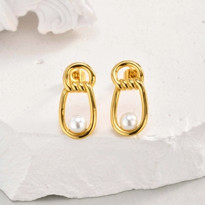 Detail of elegant gold knot earrings with glossy white pearl on stone background
