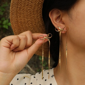 Golden bow earrings with long fringe blade chains in a stylish French outdoor setting