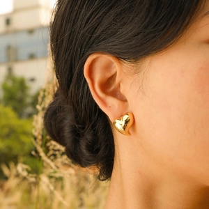 Close-up of golden heart-shaped stud earring with mirror finish on model’s ear