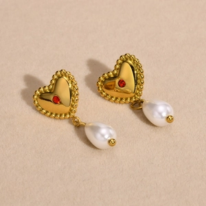 Golden heart earrings with red zircon and drop pearl on beige velvet background