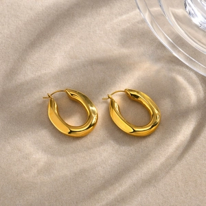 Minimalist gold U-shaped chunky hoop earrings on sand with textured glass
