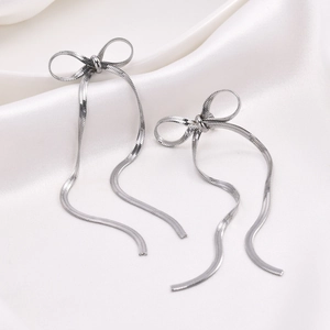 Close-up of silver bow tassel earrings with snake chain detail on white silk