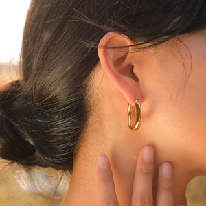Polished gold-plated U-shaped chunky hoop earrings for women worn in natural sunlight