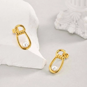 Detail of elegant gold twist earrings with white pearls on a minimalist stone display