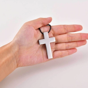 Detailansicht eines minimalistischen Kreuzanhängers aus Edelstahl in der Hand gehalten