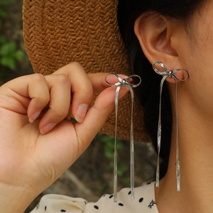 Detail showing elegant silver bow earrings with flowing snake chain tassels worn outdoors