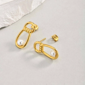 Detail of gold oval hoop earrings featuring white pearls and twisted metal craftsmanship