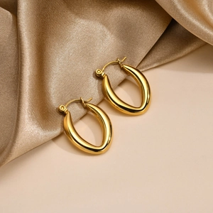 Detailed close-up of gold-plated U-shaped drop earrings on elegant champagne silk fabric