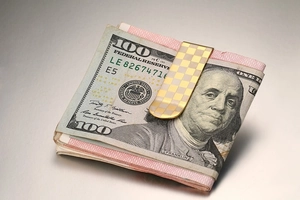 Detail of checkered gold and silver money clip securing 100 dollar bills in a macro shot