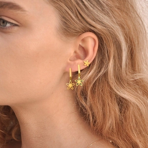 Close-up of golden stainless steel floral earrings set worn by a female model