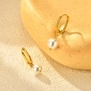 Détail de boucles d'oreilles ovales dorées avec pendentifs en perles sur surface texturée