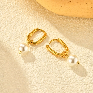 Boucles d'oreilles ovales dorées avec perles blanches sur une surface texturée chic
