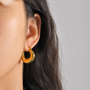 Close-up of polished gold-plated thick C-shaped hoop earrings on a female model