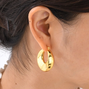 Close-up of a model wearing wide gold C-shaped hoop earrings with a polished finish