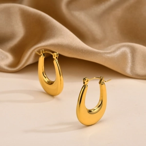 Detailed view of chunky golden U-shaped hoop earrings on elegant champagne silk fabric