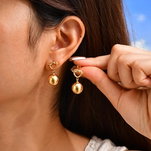 Close-up of 18K gold-plated knotted heart and hollow bead earrings worn by a model