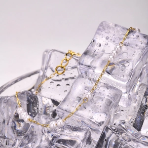 Golden paperclip chain anklet with round white pearls on creative ice cubes background