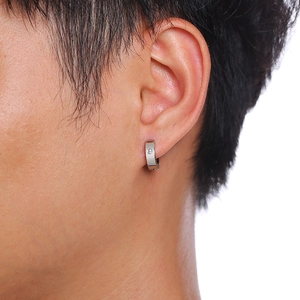 Gros plan d'une créole en acier inoxydable argenté poli avec un petit zircon sur l'oreille
