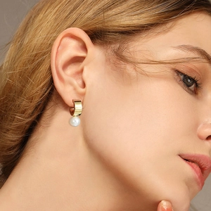 Elegant gold C-shaped hoop earrings with dangling pearls worn by a female model