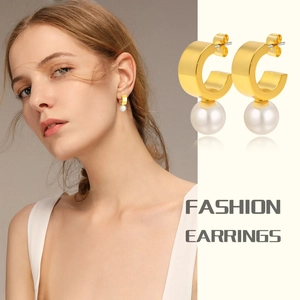 Detail of C-shaped gold-plated copper earrings with white round pearl pendants