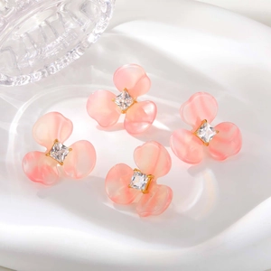 Détail de quatre boucles d'oreilles fleurs en résine rose avec zircon carré en bol blanc