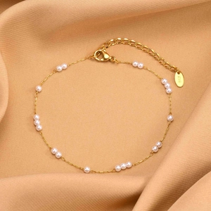Macro detail of gold-plated stainless steel anklet with pearls and K18 hallmark tag
