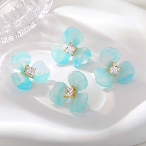 Détail des boucles d'oreilles fleur en résine bleue avec zircon cubique carré doré