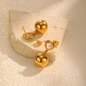 Minimalist 18K gold plated knotted heart and hollow bead earrings on a stone pedestal