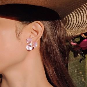 Détail d'une boucle d'oreille fleur en résine rose avec zircon carré sur une oreille