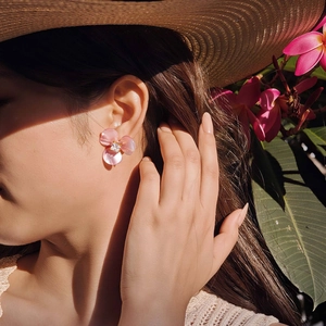 Gros plan sur boucle d'oreille fleur en résine rose et zircon sur fond tropical d'été