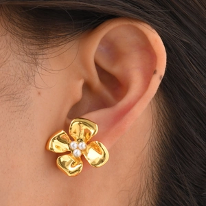 Close-up of gold flower earring featuring three white pearls on a female model's ear