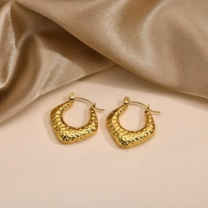 Detailed close-up of gold irregular hammered texture hoop earrings on silk fabric