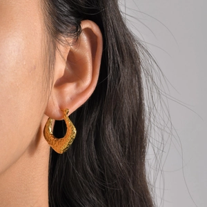 Close-up of golden U-shaped hammered earrings showing textured metal finish on ear
