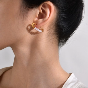 Detailed close-up of golden safety pin earrings with elegant pearls worn by a model