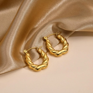 Close-up of golden U-shaped twisted chain hoop earrings on elegant silk fabric