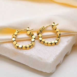 Vue détaillée des boucles d'oreilles dorées perlées avec finition polie sur marbre