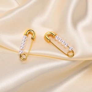Elegant golden safety pin earrings with pearls on luxury champagne silk fabric