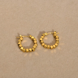 Boucles d'oreilles créoles à perles carrées dorées en acier sur fond beige doux