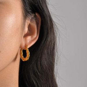 Close-up of golden U-shaped twisted hoop earrings on model showing rope texture
