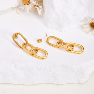 Détail des boucles d'oreilles à triple maillons dorés présentées sur un socle en pierre